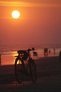 Silhouette bicycle on beach against sky during sunset