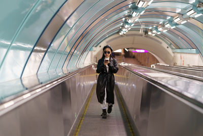 Japanese girl blogger in trendy trench and glasses on escalator use smartphone read follower comment