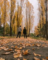 Rear view of people walking on leaves during autumn