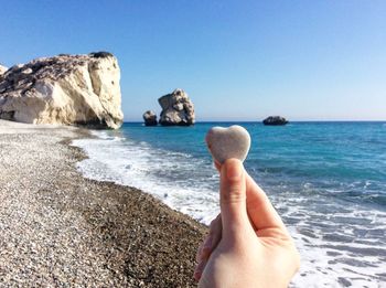 Close-up of hand holding rock in sea against clear sky