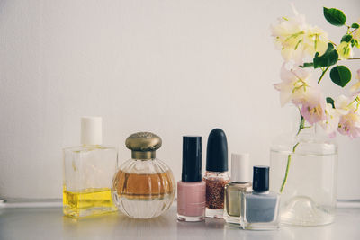 Beauty products arranged by flower vase on table against white wall