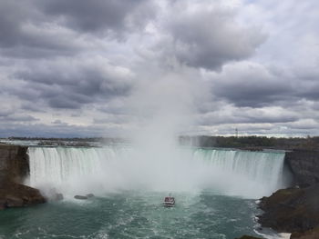 Scenic view of waterfall against cloudy sky