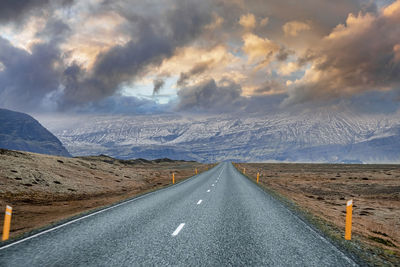 Diminishing road leading towards mountain range against cloudy sky at sunset