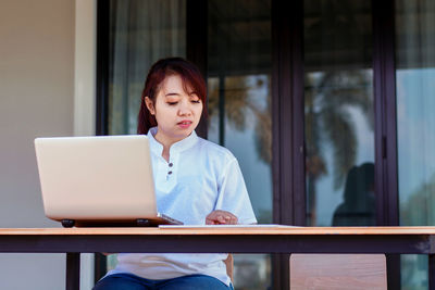 Mid adult woman using mobile phone while sitting on table