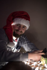 Smiling young man wearing santa hat with illuminated string lights at home