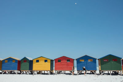 Beach huts by buildings against clear blue sky