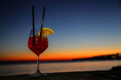 Close-up of water drop hanging on sea against sky during sunset