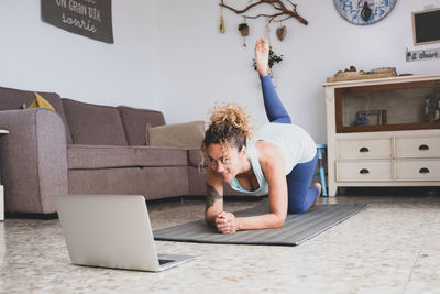 Smiling woman looking at laptop while exercising at home