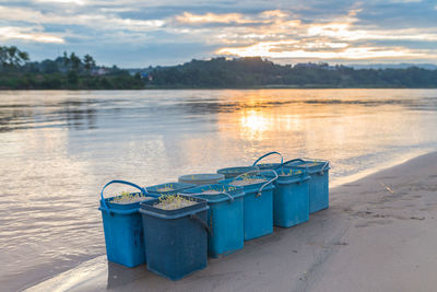 Deck chairs on shore against sky during sunset