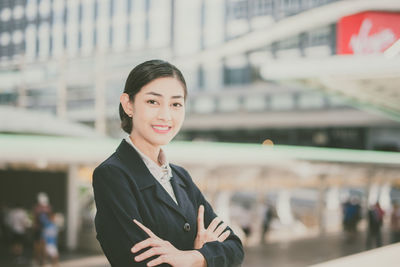 Portrait of businesswoman with arms crossed standing against buildings in city