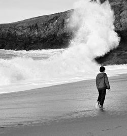 Rear view of boy walking on shore at beach