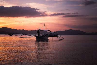 Outrigger in sea against sky during sunset