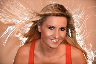 Portrait of smiling young woman with blond hair against brown background