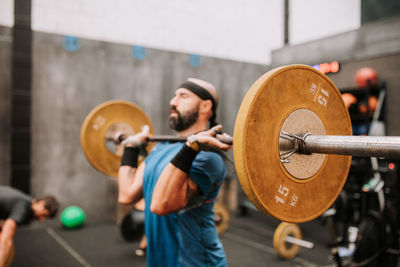 Side view of muscular male athlete doing clean and jerk exercise while training in modern fitness center