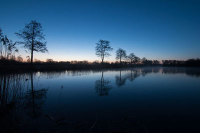 Scenic view of silhouette trees by lake against sky at night