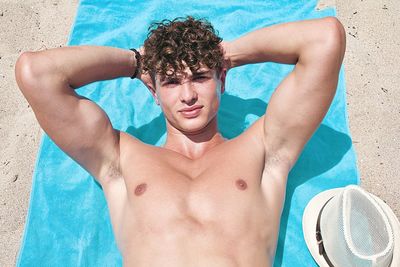 Shirtless man relaxing at beach in sunny day