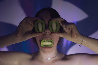 Close-up of woman covering eyes with kiwi slices in darkroom