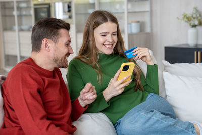 Young couple using credit card and smartphone for online shopping on internet sites sitting at home