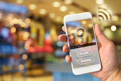 Close-up of hand holding smart phone against illuminated lights