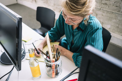 High angle view of confident female it professional writing on note pad at desk in creative office