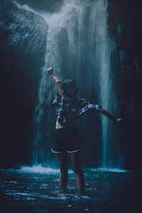 Woman with arms outstretched standing against waterfall