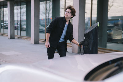 Young man pulling out electric plug at charging station