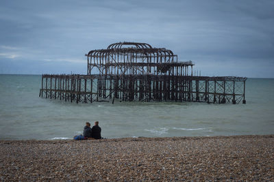 Rear view of woman sitting on beach against sky