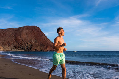 Full length of shirtless man standing at beach against sky