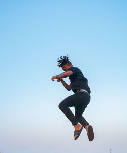 Full length of young man jumping against clear sky