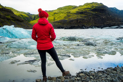 Rear view of woman standing on rock by frozen river