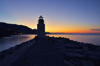 Lighthouse by sea against sky during sunset