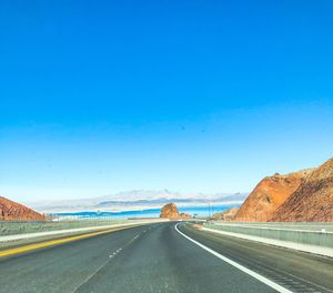 Road leading towards mountains against clear blue sky