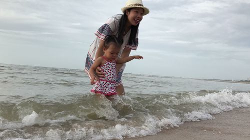 Mother and daughter wading in sea against sky