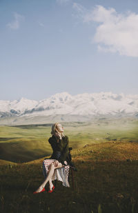 Beautiful woman sitting on chair while looking away against cloudy sky