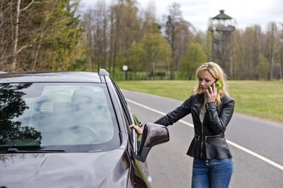 Woman using smart phone while standing by car