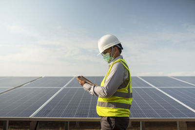 Rear view of man standing on solar panel against sky