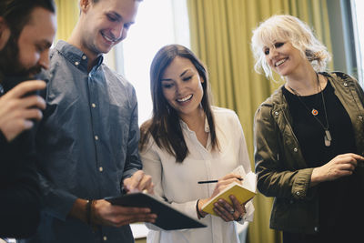 Happy business people using digital tablet together while standing in board room