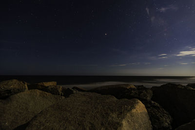 Scenic view of rocks at sea against sky at night