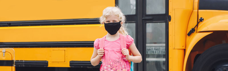 Back to school. girl student wearing face mask near yellow bus. web banner header.