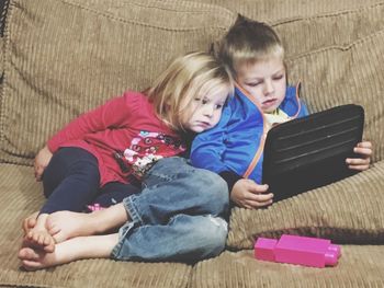 Full length of siblings looking at digital tablet while sitting on sofa