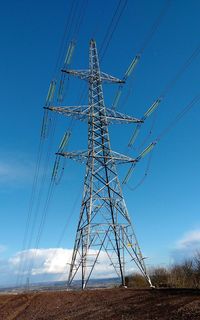 Low angle view of electricity pylon against blue sky