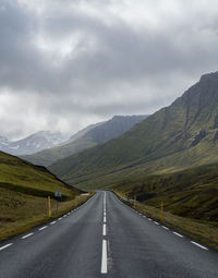 Empty road leading towards mountains against sky