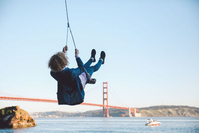 Rear view of mid adult woman swinging at beach against sky