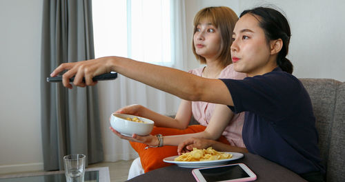 Young women watching tv while sitting with food on table