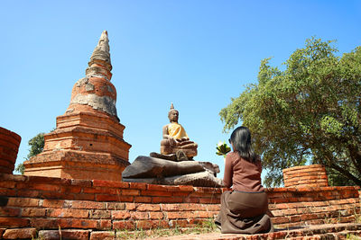 Woman praying in front of buddha image at wat phra ngam temple ruins in ayutthaya, thailand