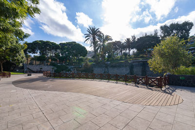 Footpath by swimming pool in park against sky