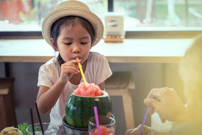 Cute girl drinking watermelon juice with straw in restaurant