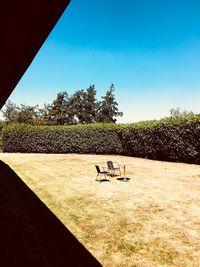 Park bench on field against clear blue sky