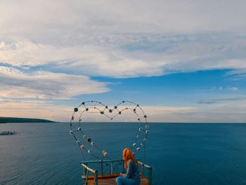 Rear view of man by sea against sky during sunset