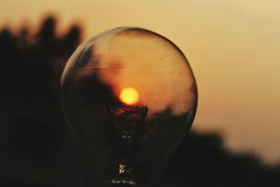 Close-up of illuminated light bulb against sunset sky